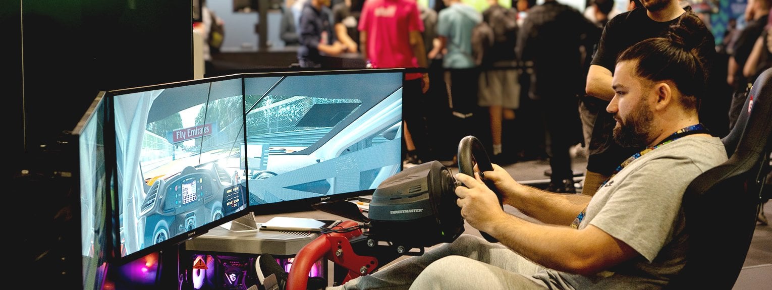 A man playing a driving simulator game on a Cyberpower simulator PC at the London EGX festival with one of our staff members behind him. 